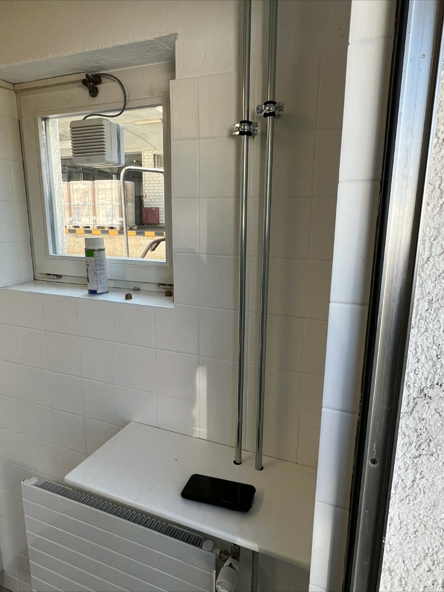 Heizkörper mit Rohrleitungen – Kompaktheizkörper mit verchromten Steigleitungen und Thermostatventil. Saubere Installation in renoviertem Raum.