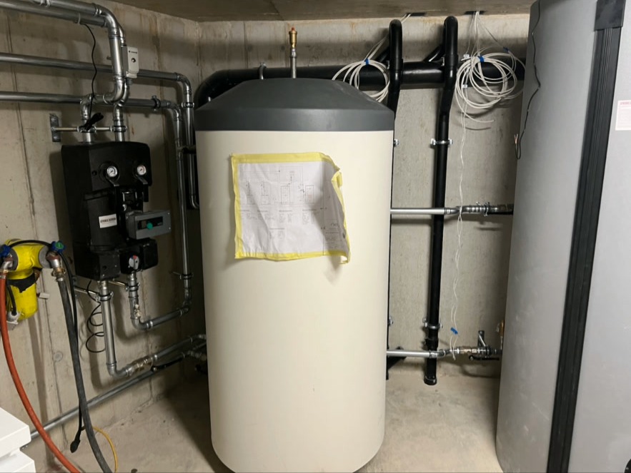 Warmwasserspeicher mit Anschlüssen – Grosser Warmwasserspeicher mit Pumpengruppe, Rohrleitungen und Sensoranschlüssen. Fachgerechte Installation im Neubau.