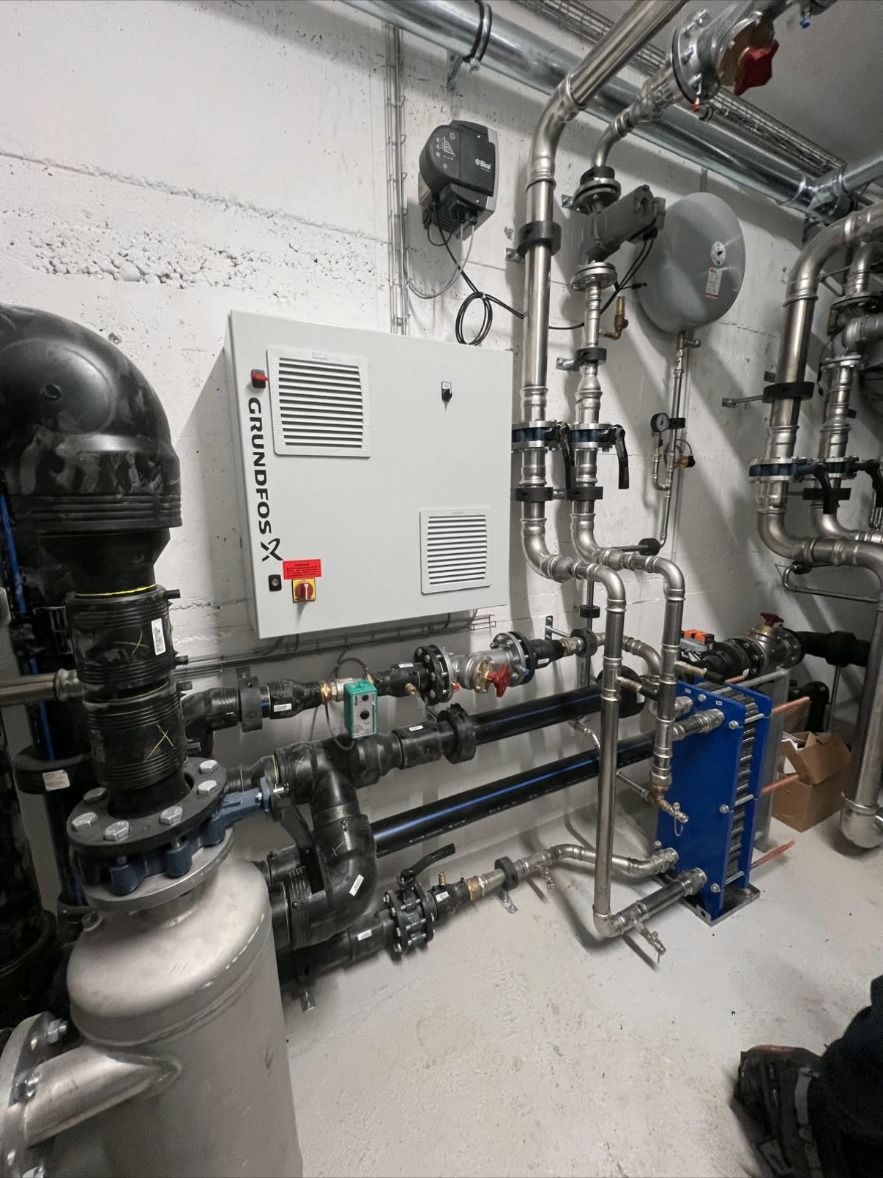 Grundfos Steuerung & Plattenwärmetauscher – Technikraum mit Grundfos Steuerung, Plattenwärmetauscher und präzise verlegten Edelstahlleitungen für effiziente Wärmeübertragung.